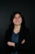 „Porträt einer lächelnden Frau mit dunklen schulterlangen Haaren vor dunklem Hintergrund, die mit verschränkten Armen in die Kamera blickt.“ Businessportrait im Fotostudio
