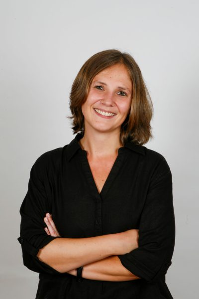 Businessfoto einer jungen Frau mir braunen mittellangen Haaren, freundlichem offenen Lächeln. Fotostudioaufnahme mit grauem Hintergrund in Göttingen