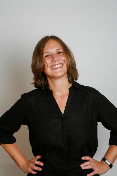 Businessfoto einer jungen Frau mir braunen mittellangen Haaren, freundlichem offenen Lächeln. Fotostudioaufnahme mit grauem Hintergrund in Göttingen