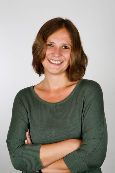 Businessfoto einer jungen Frau mir braunen mittellangen Haaren, freundlichem offenen Lächeln. Fotostudioaufnahme mit grauem Hintergrund in Göttingen