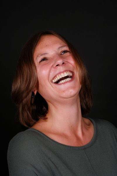 Businessfoto einer jungen Frau mir braunen mittellangen Haaren, freundlichem offenen Lächeln. Fotostudioaufnahme mit grauem Hintergrund in Göttingen