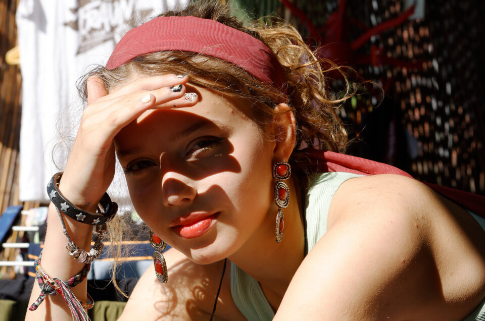 junge Frau auf dem Balkon, elegant geschminkt in einem Hotel. Sie steht in der prallen Sonne und schützt sich die Augen mit der Hand, was spannende Schatten ins Gesicht wirft. Fotoshooting