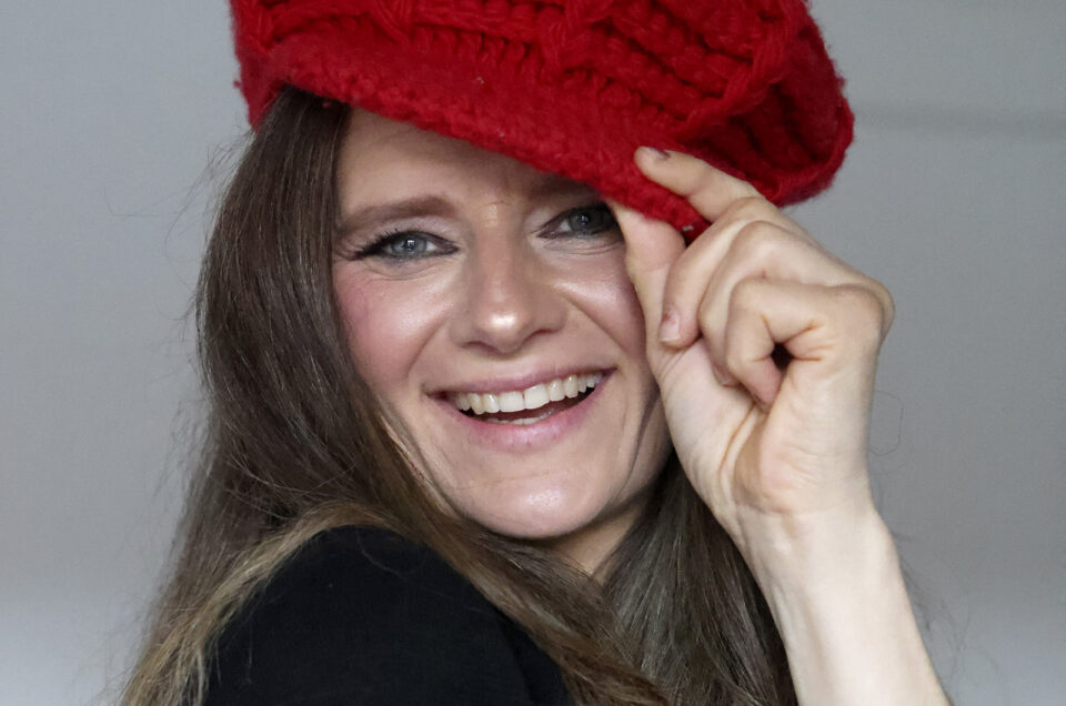Ein Selbstportrait von mir selbst der Fotografin mit professionellem Make-up und Hairstyling. Roter Mütze. Lächeln in die Kamera. Langes glkattes mittelblondes Haar.